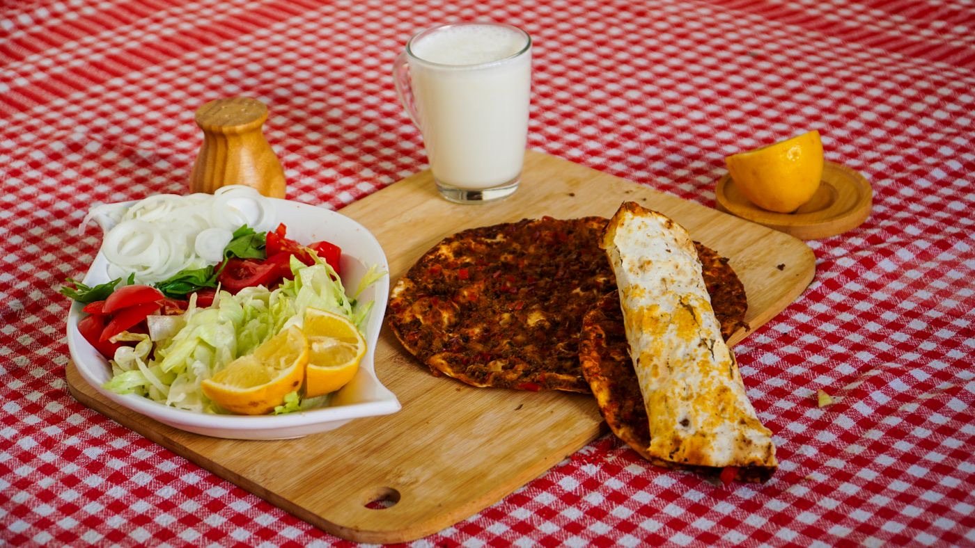 A glass of frothy ayran served alongside Turkish lahmacun, salad and lemon